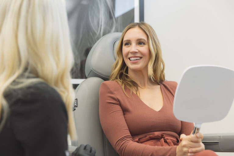 woman holding a mirror and smiling after sculptra in Oklahoma City