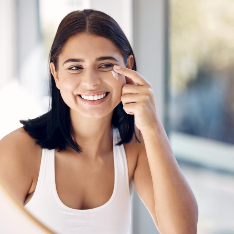 Woman smiling in the mirror using the best facial sunscreen in Oklahoma City