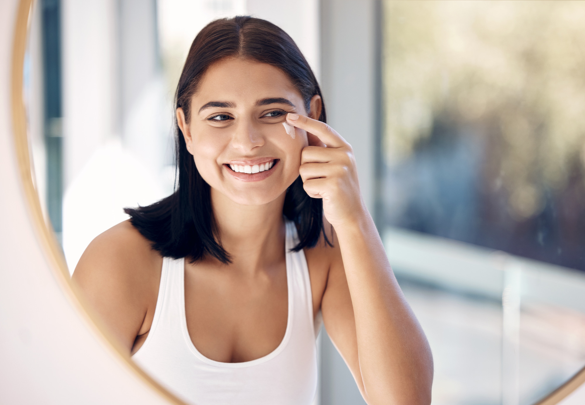 Woman smiling in the mirror using the best facial sunscreen in Oklahoma City